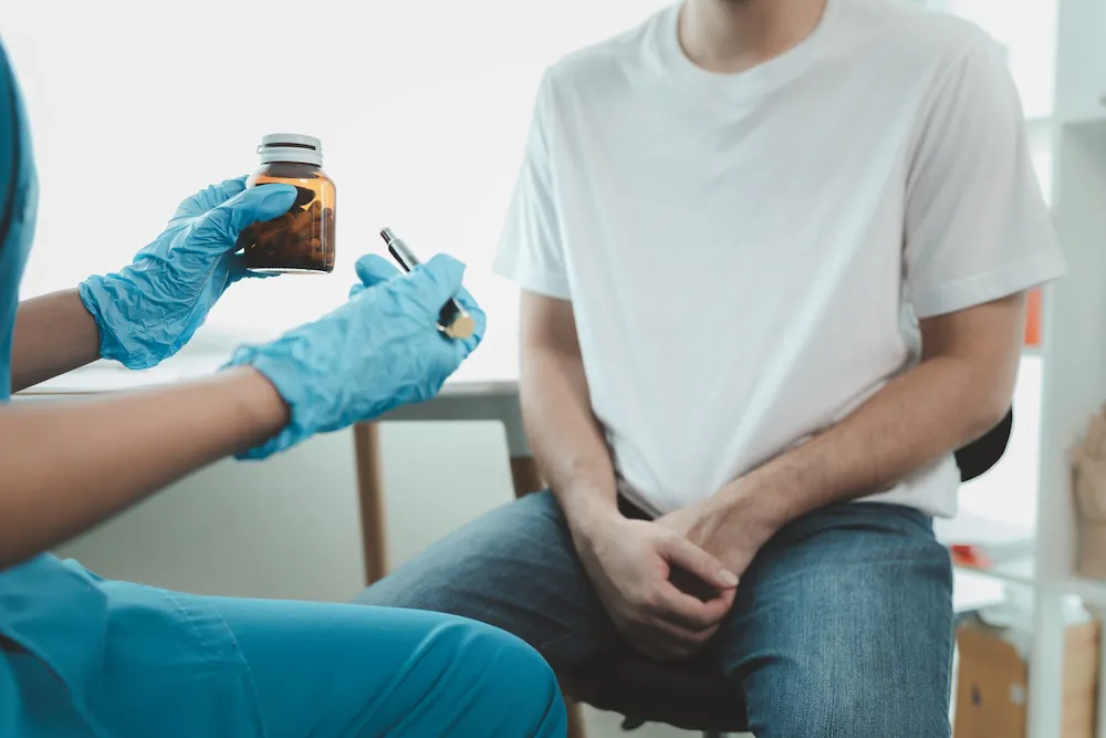 A healthcare professional holding a prescription bottle and discussing medication with a male patient.