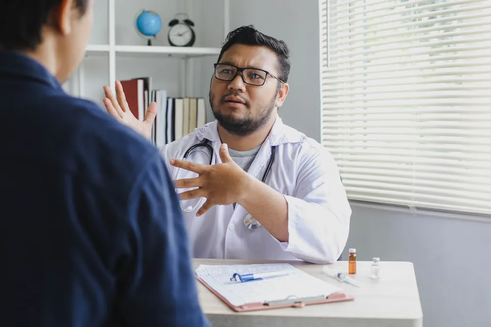A doctor in a white coat explaining something to a patient during a consultation.